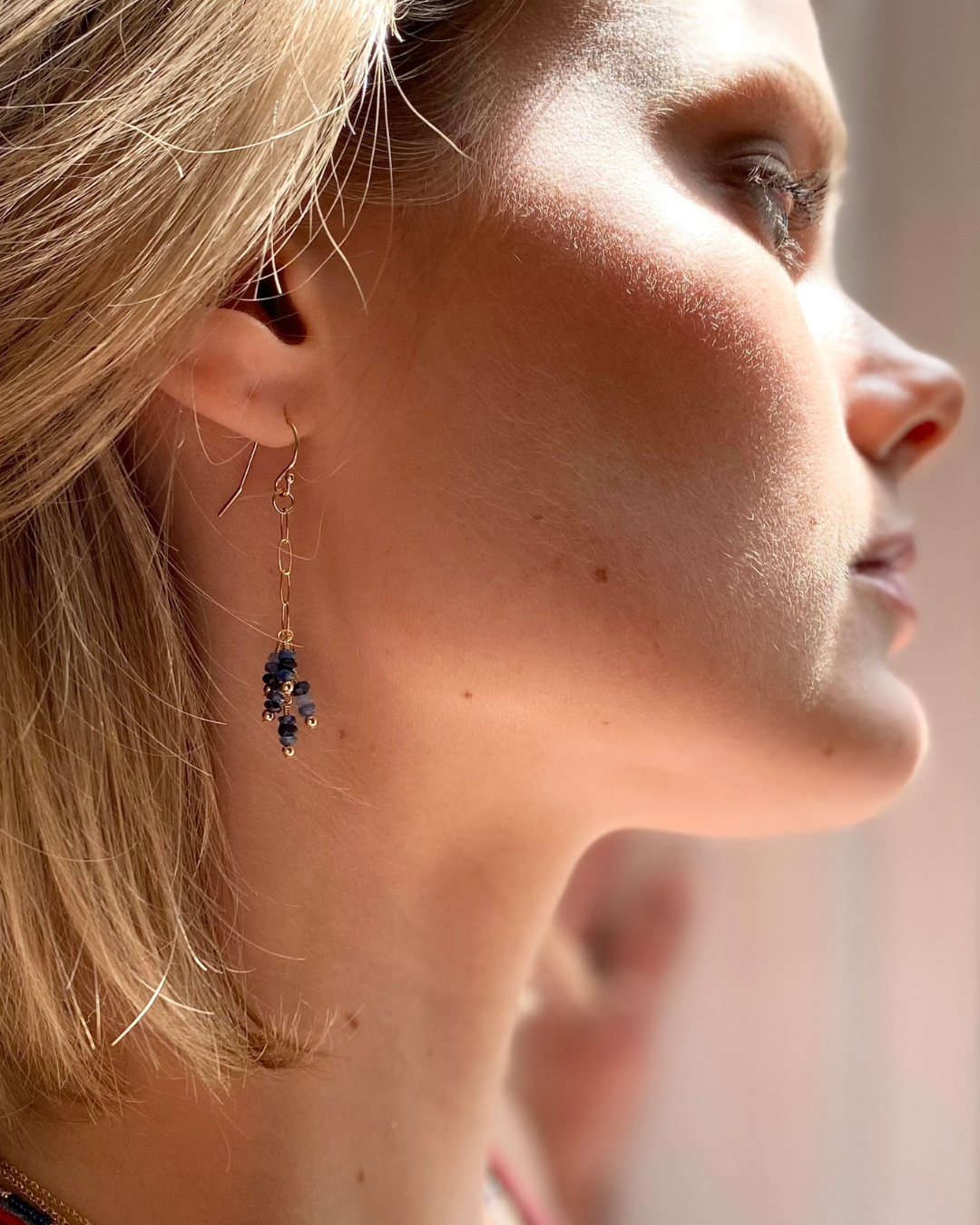 Close-up of a woman wearing a gold earring with blue sapphire gemstones.