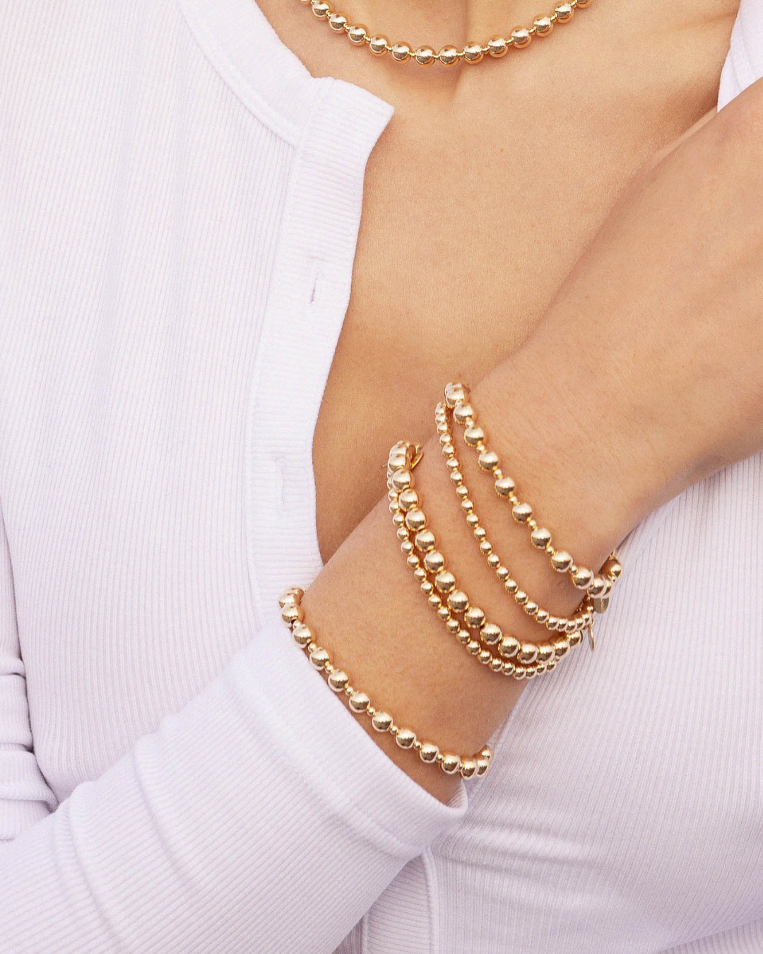 Gold beaded bracelets on a person's wrist wearing a long sleeved white top