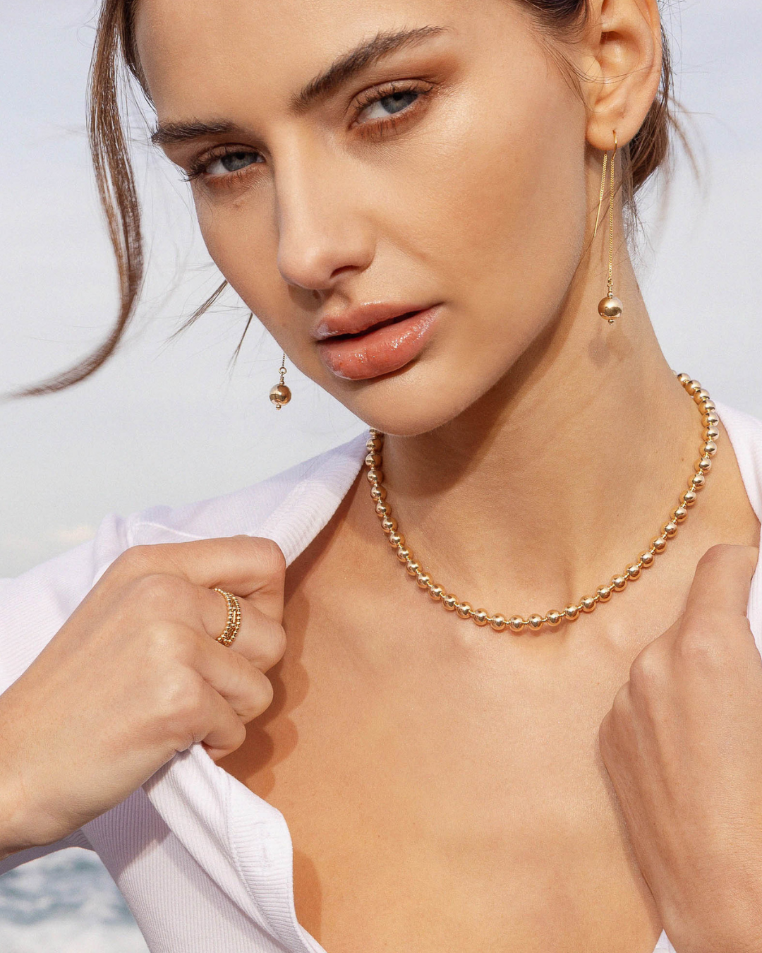 Woman wearing gold jewellery including a necklace, earrings, and rings against a light background