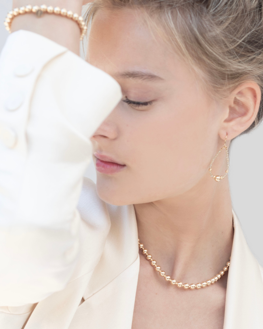 Close-up of a person wearing a gold necklace and earrings with a blurred background