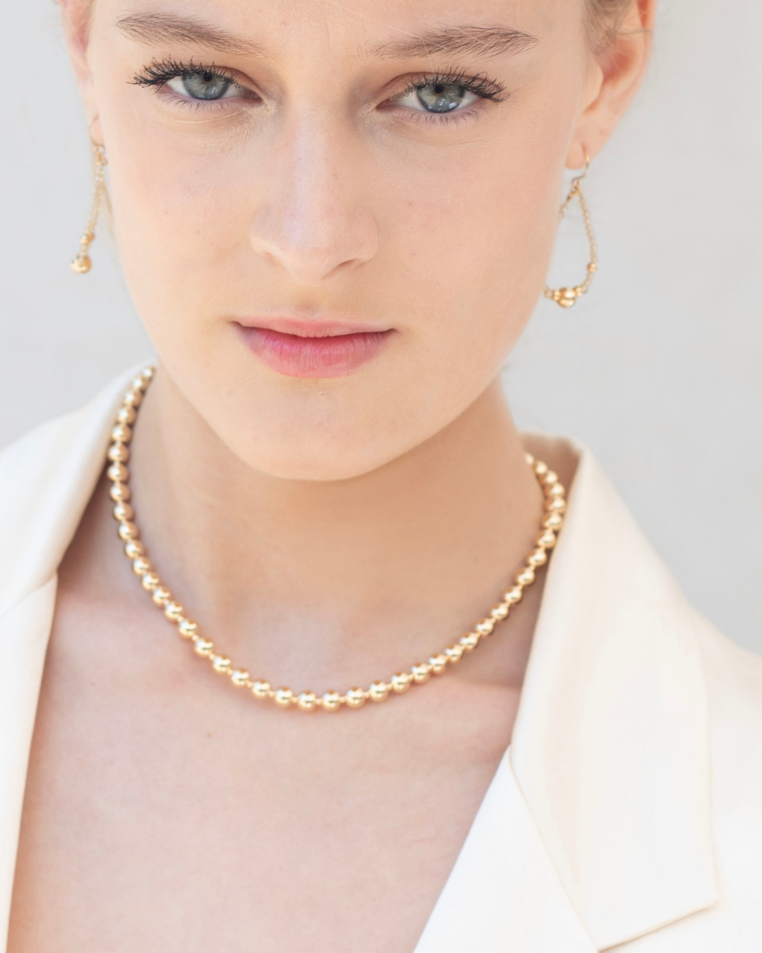 Woman wearing a gold necklace and zircon earrings on a light background