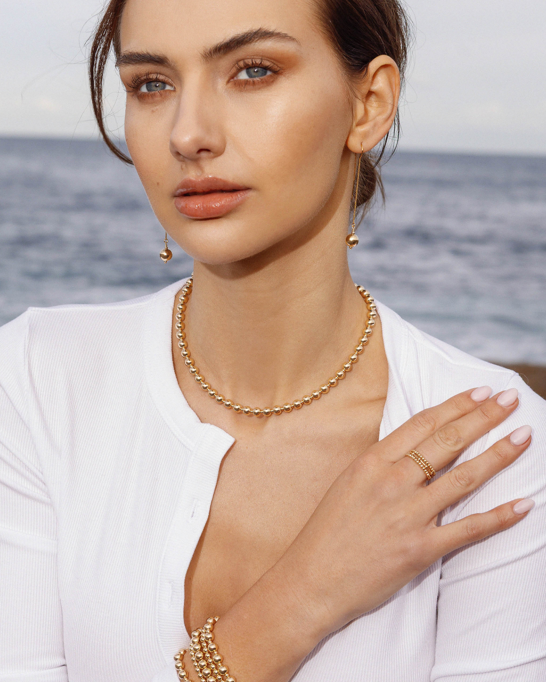 Woman wearing gold jewellery with a blurred ocean background