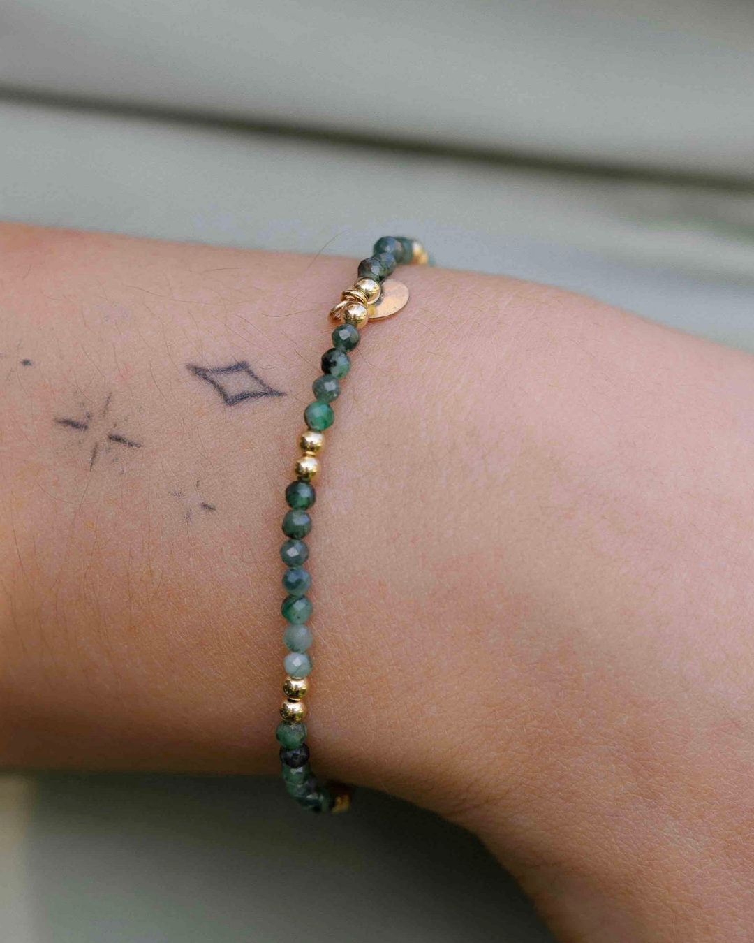 Gold emerald beaded bracelet on a wrist with a neutral background