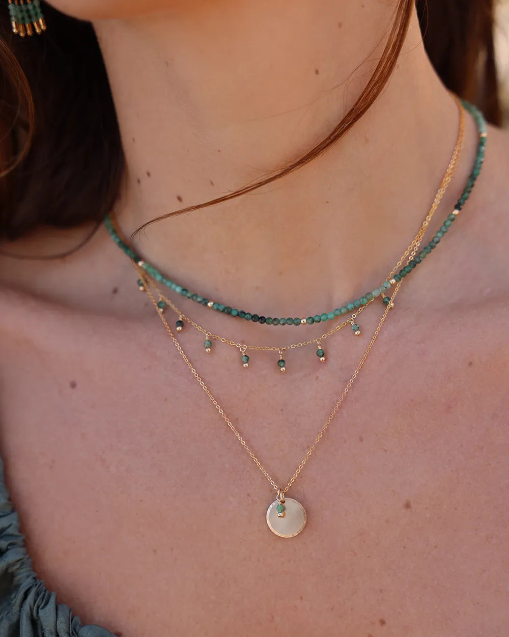 Model wearing necklace with Emerald gems in shades of green, complemented by gold accent beads