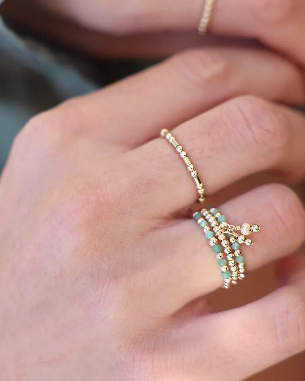 Gold and emerald beaded rings on a finger against a neutral background