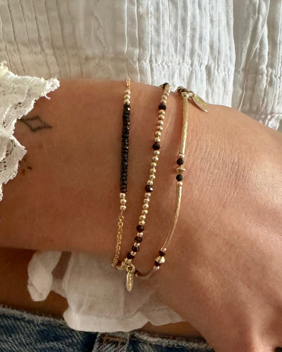 Close-up of a wrist wearing multiple gold and black gemstone beaded bracelets on a light background