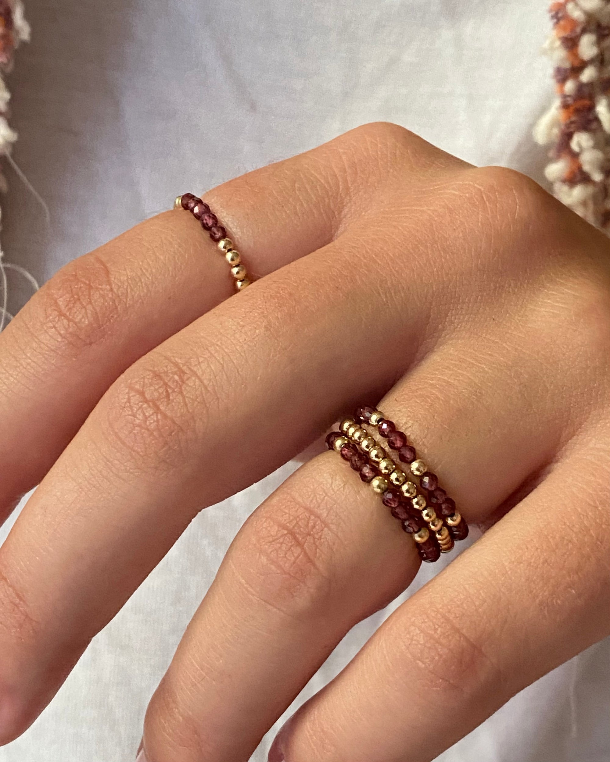 Close-up of a hand wearing two gold and garnet beaded rings on a light background