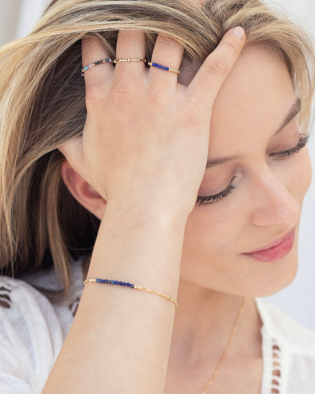 Woman wearing a fine gold bracelet with lapis lazuli gemstones and multiple rings with a neutral background