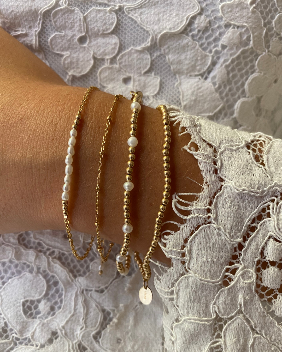 Two gold and pearl bracelets layered with two gold bracelets on a wrist with a lace top