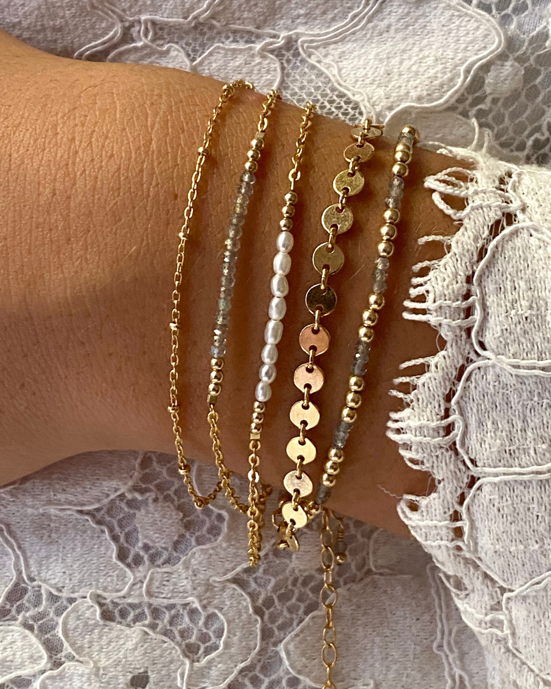 Close-up of a wrist wearing multiple gold and beaded bracelets on a lace background