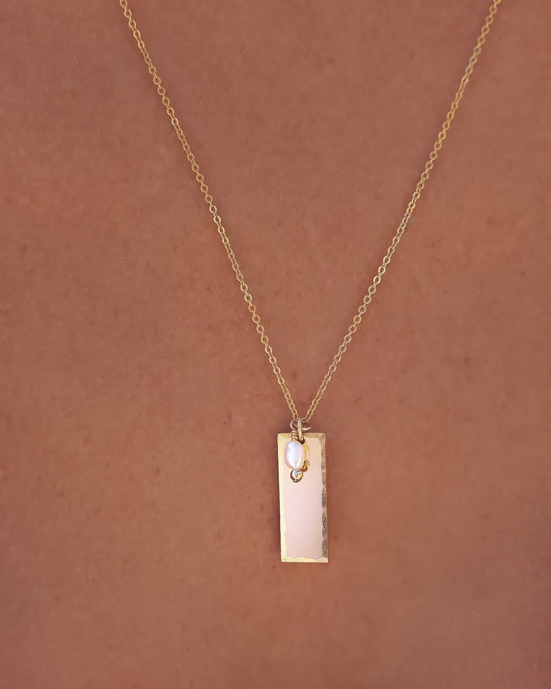 Model wearing Gold necklace with a rectangular pendant and pearl drop