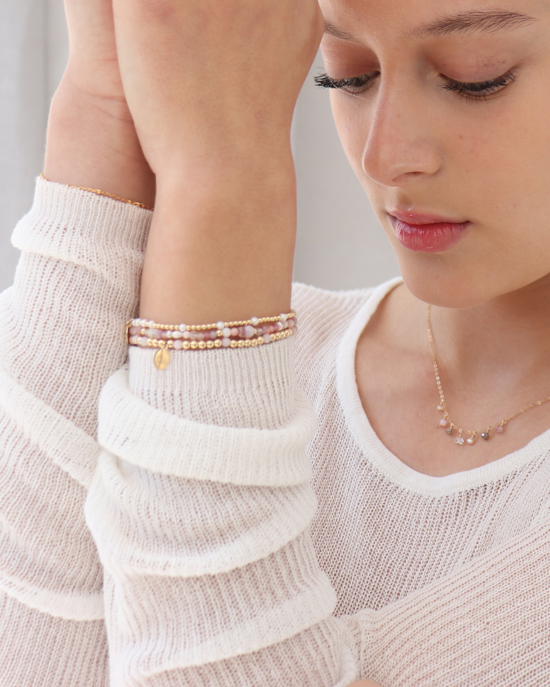 Close-up of a woman wearing multiple bracelets with pink gemstones and pearls and a fine gemstone necklace