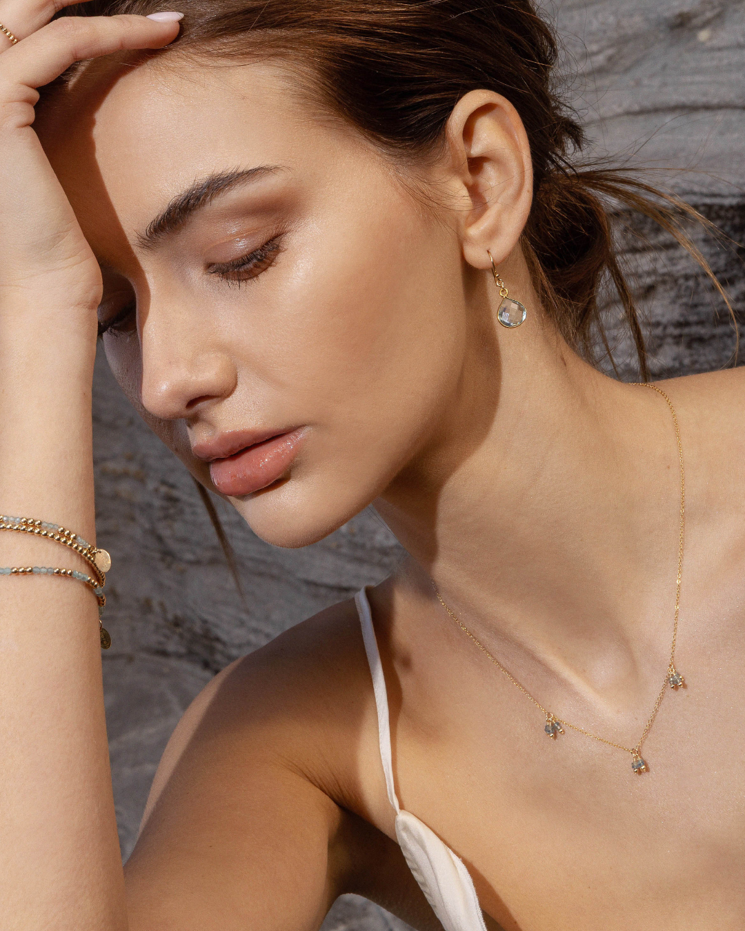 Close-up of a woman wearing gold aquamarine jewellery against a stone wall background