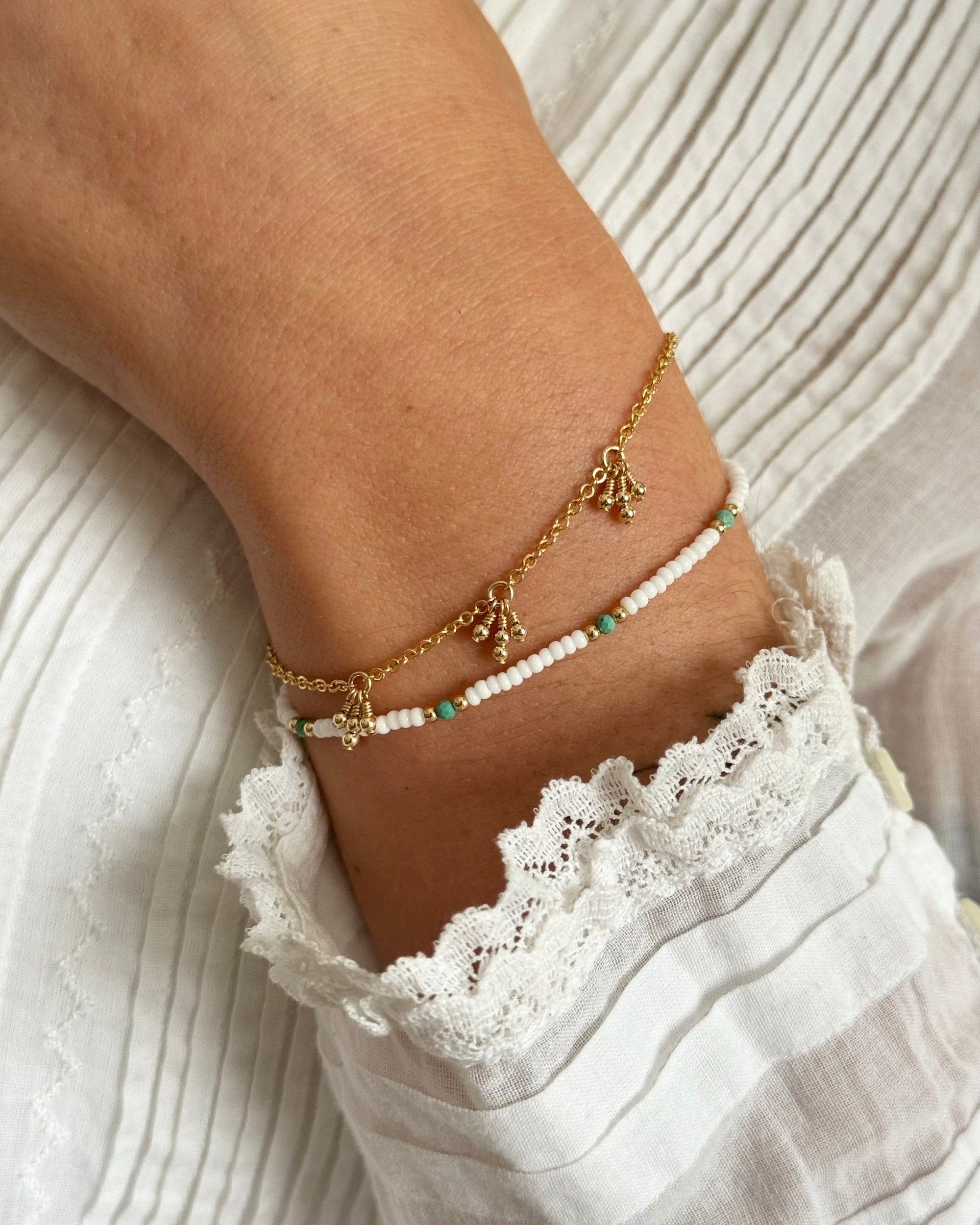 Gold bracelet with small gold beads on a person's wrist against a white lace fabric top