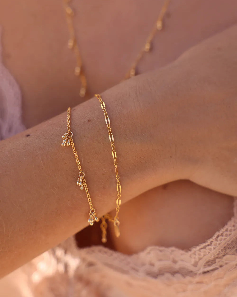 Close-up of a person's wrist wearing a bracelet with hand wire-wrapped gold tassels adorning a fine cable chain