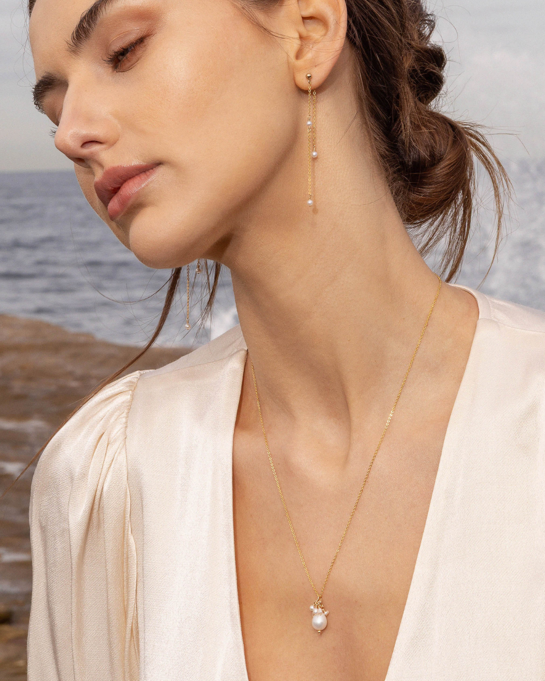 Woman wearing a gold pearl necklace and earrings with a beach background