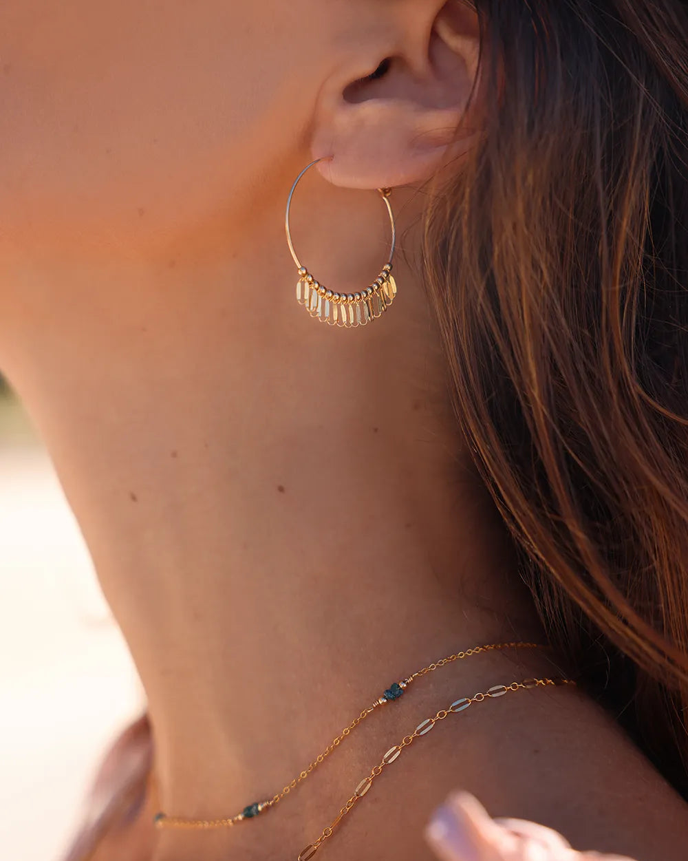 Model wearing fine gold hoop earrings accented with delicate dangle sparkle details and gold beads