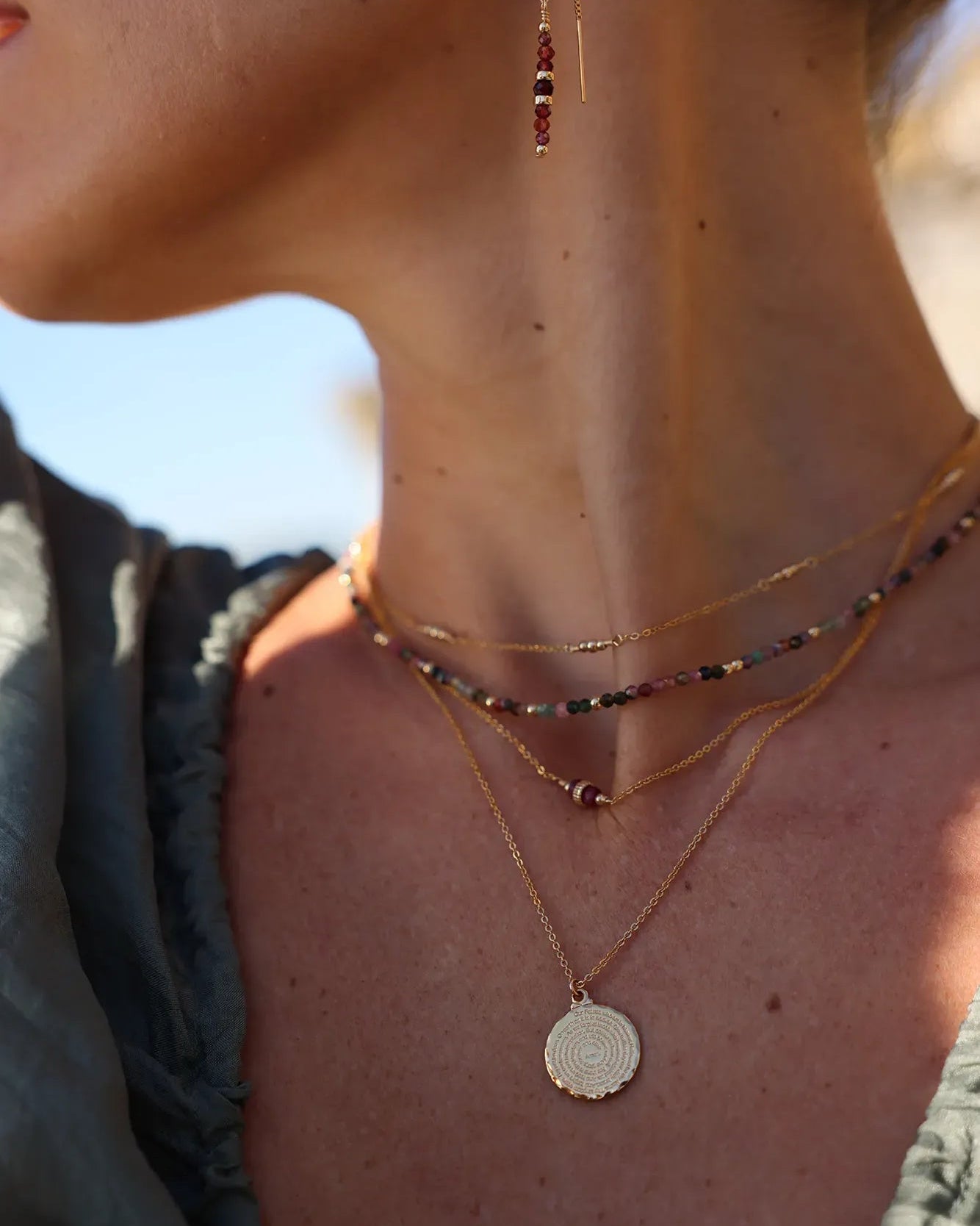 Model wearing gold necklace with a round pendant engraved with 'Our Father ...'