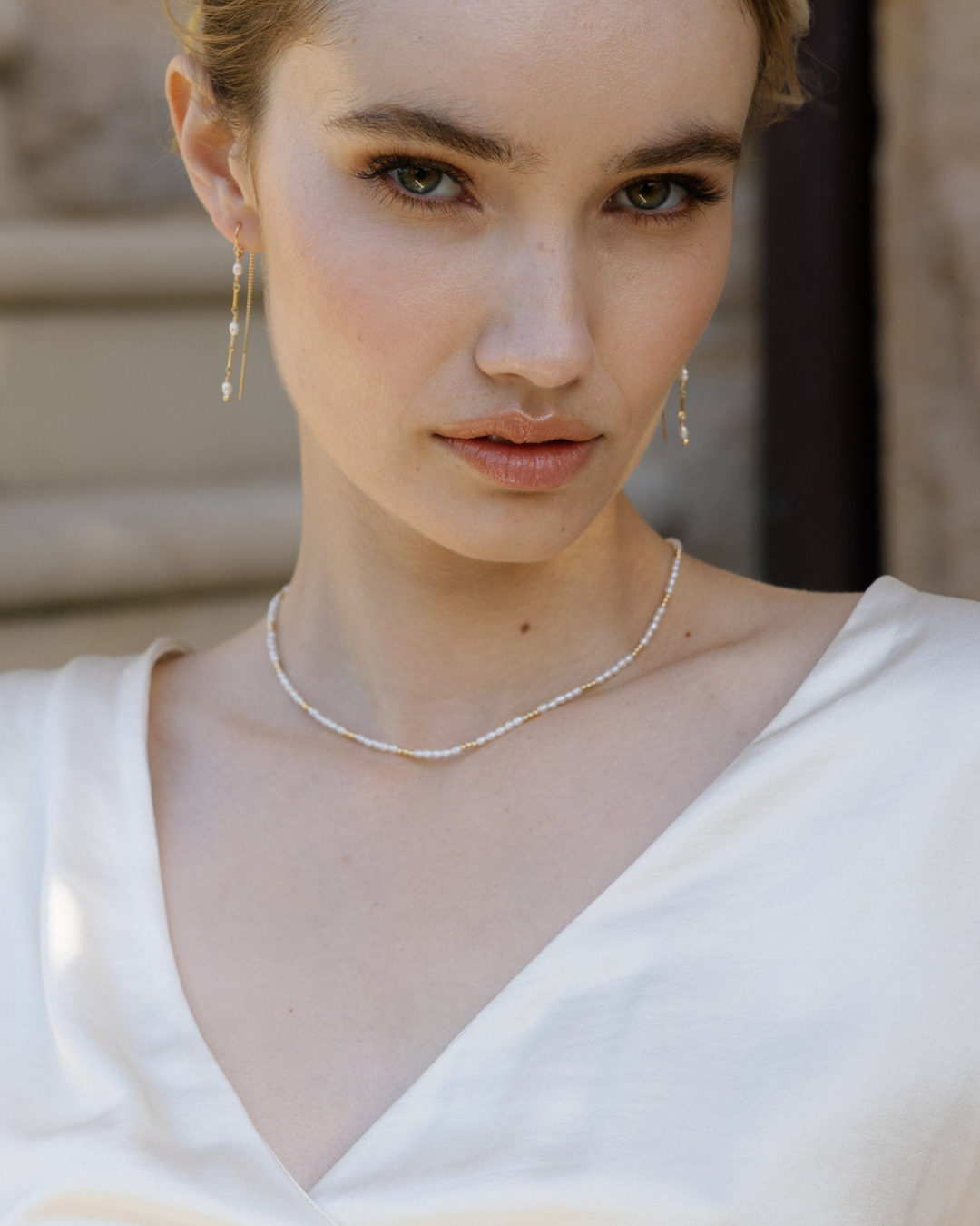 Woman wearing a gold beaded pearl necklace and earrings with a blurred background