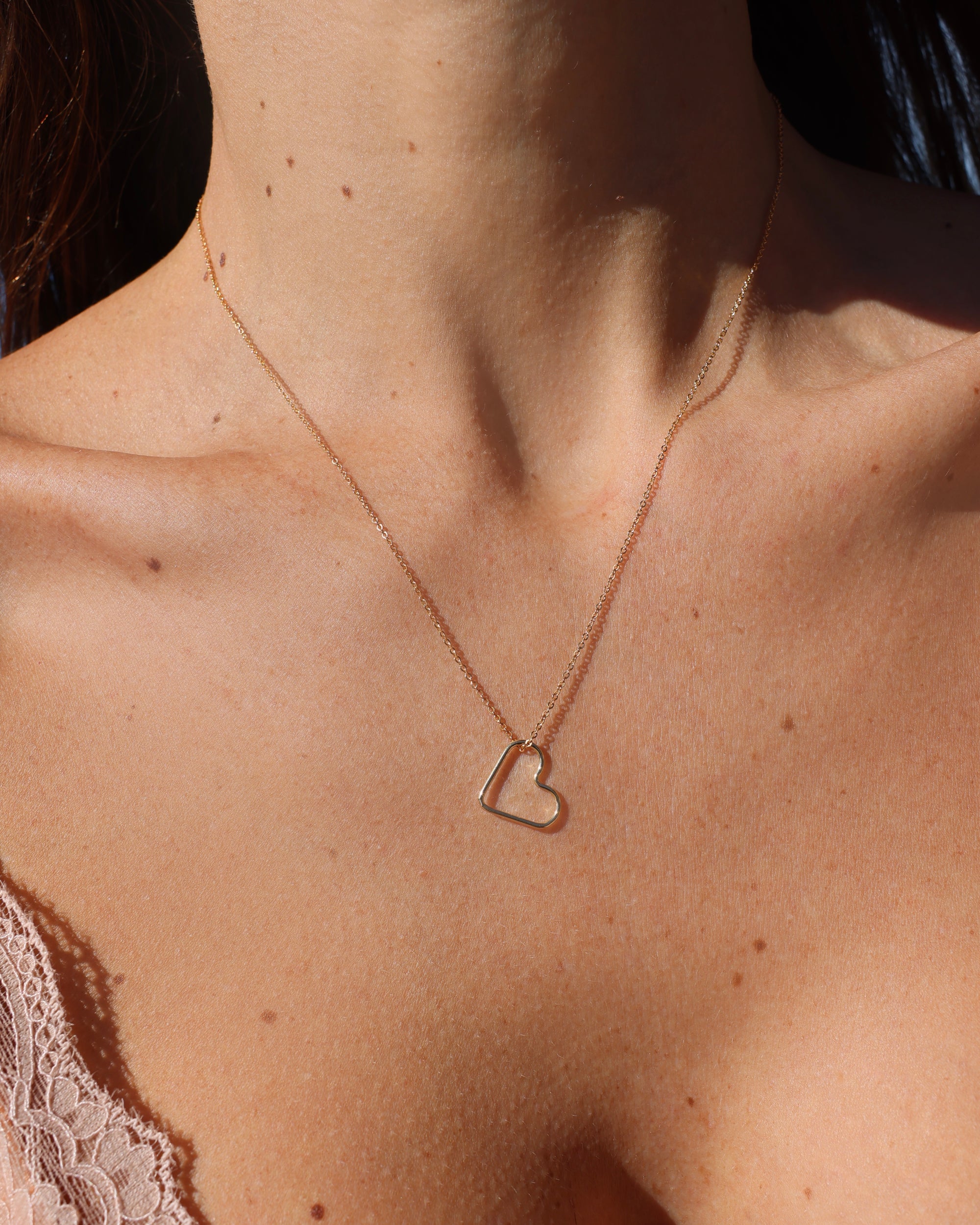 Gold heart-shaped necklace on a person's neck with a soft focus background