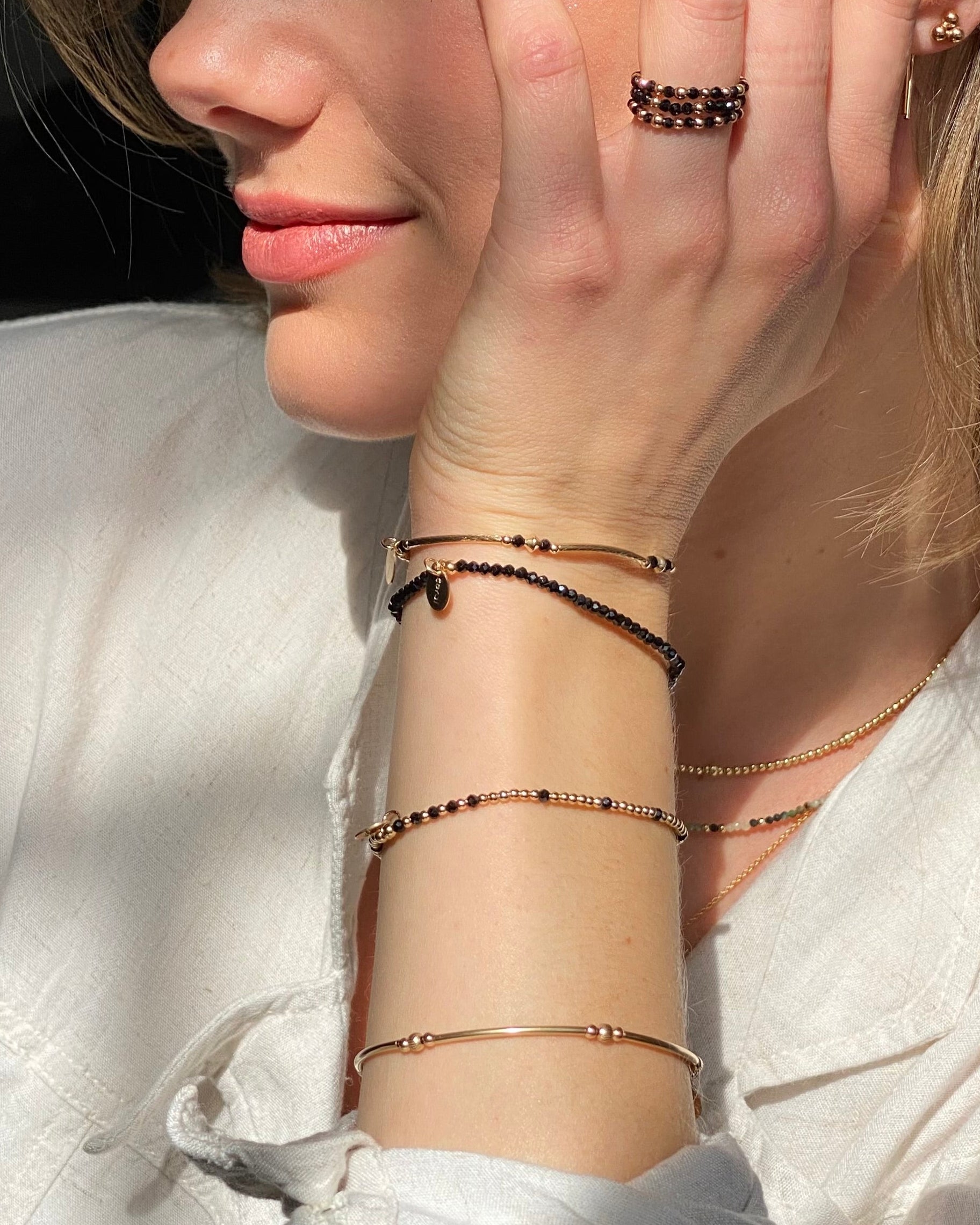 Close-up of a woman wearing multiple gold gemstone bracelets and rings wearing a white shirt