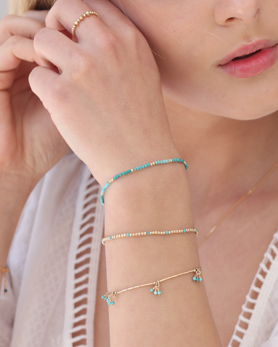 Close-up of a person wearing gold and turquoise gemstone beaded bracelets on a light background