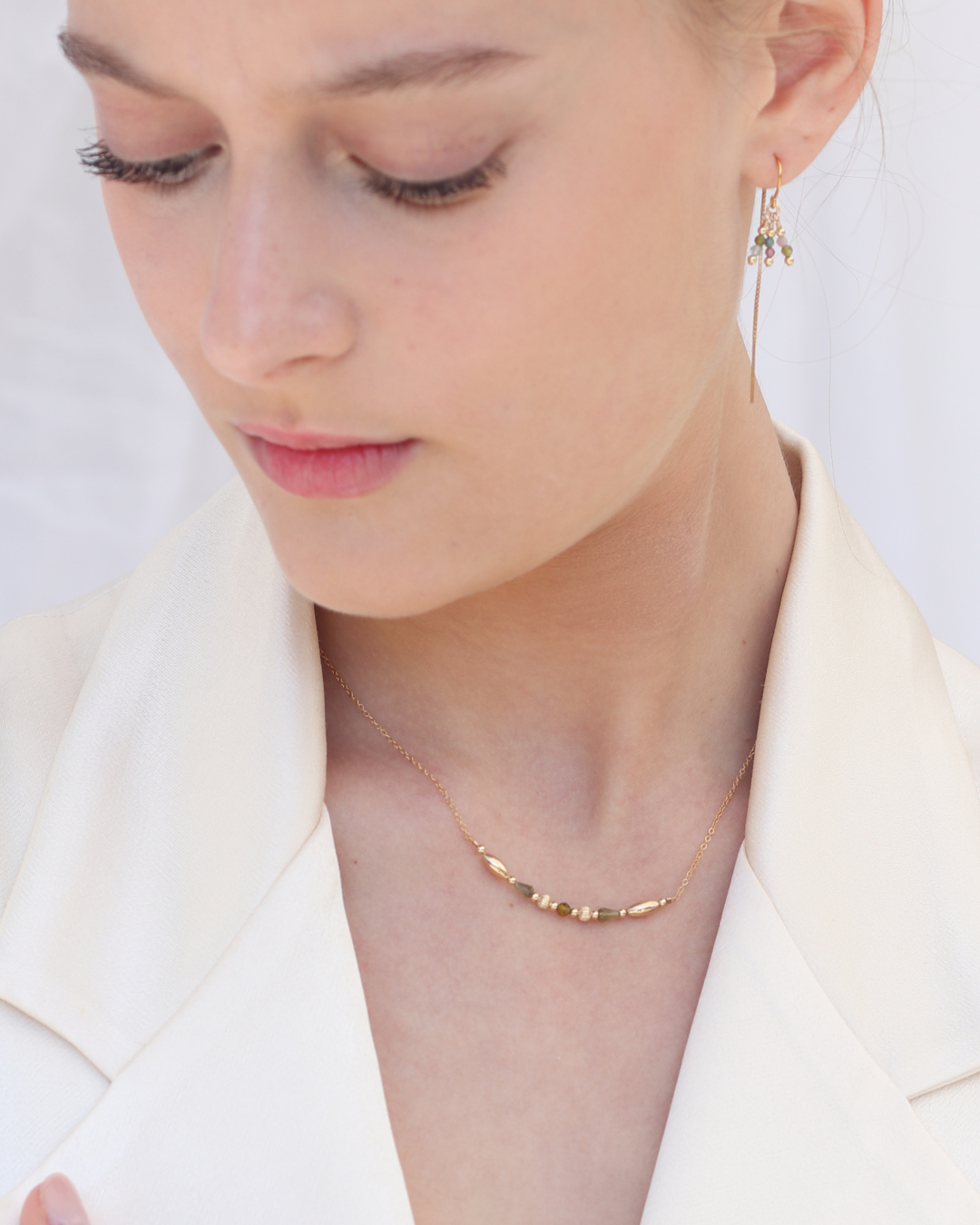 Close-up of a woman wearing gold tourmaline gemstone necklace and earrings wearing a cream blazer