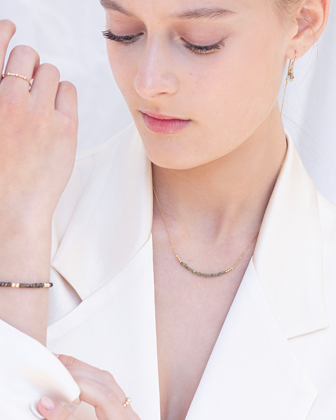 Close-up of a woman wearing gold jewellery including a necklace, bracelet, ring, and earrings on a white background.