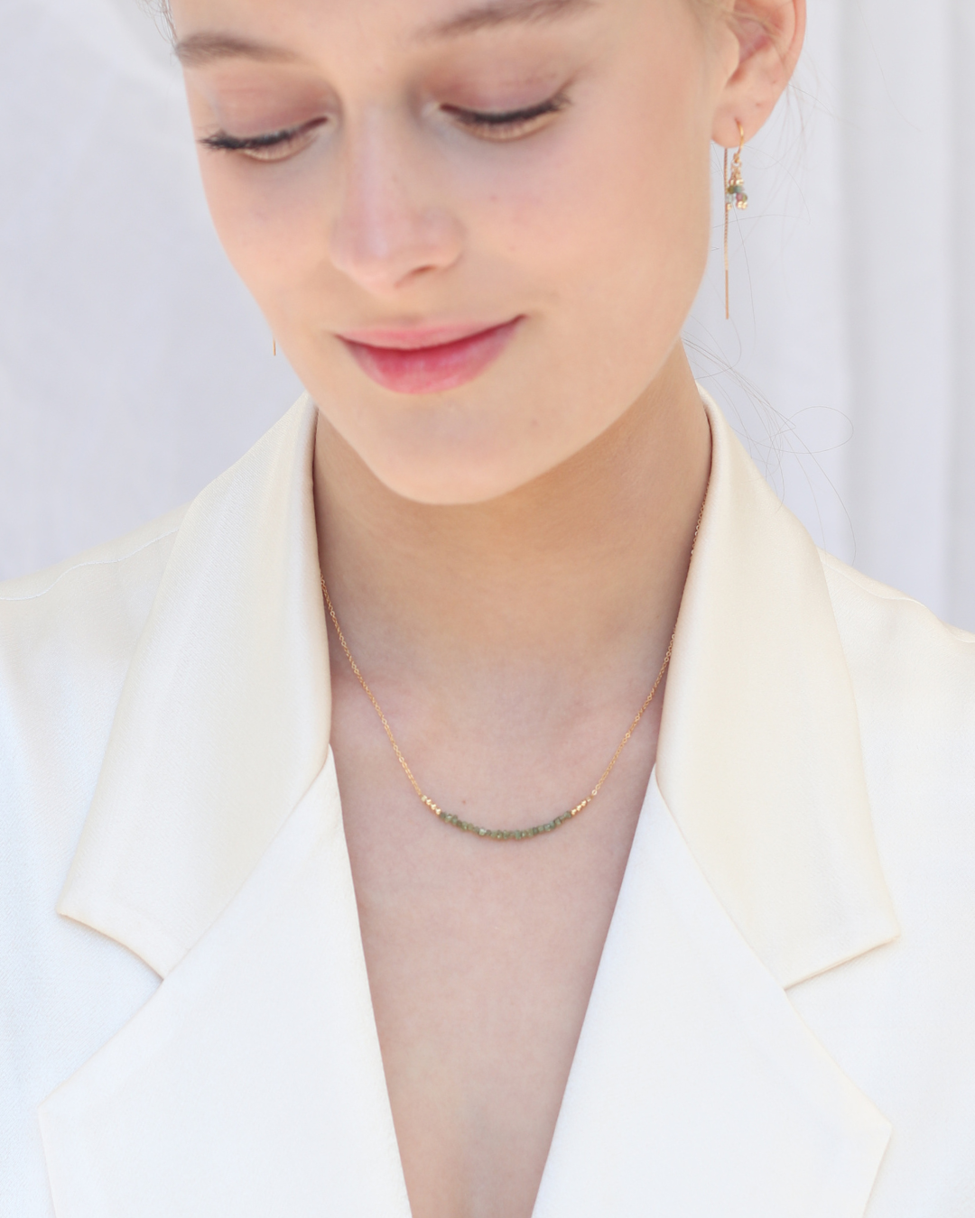 Close-up of a woman wearing a delicate necklace and earrings against a plain background