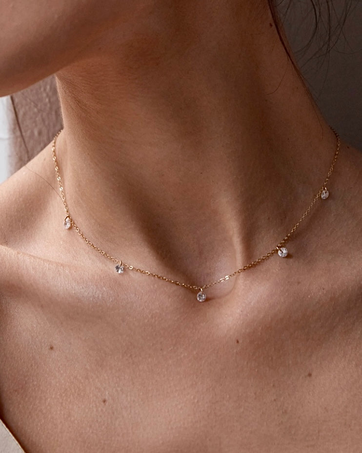 Close up of a woman's neck wearing a delicate gold necklace with cubic zirconias 