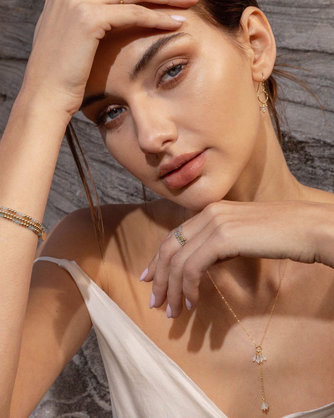 Woman wearing gold and gemstone jewellery with a neutral background