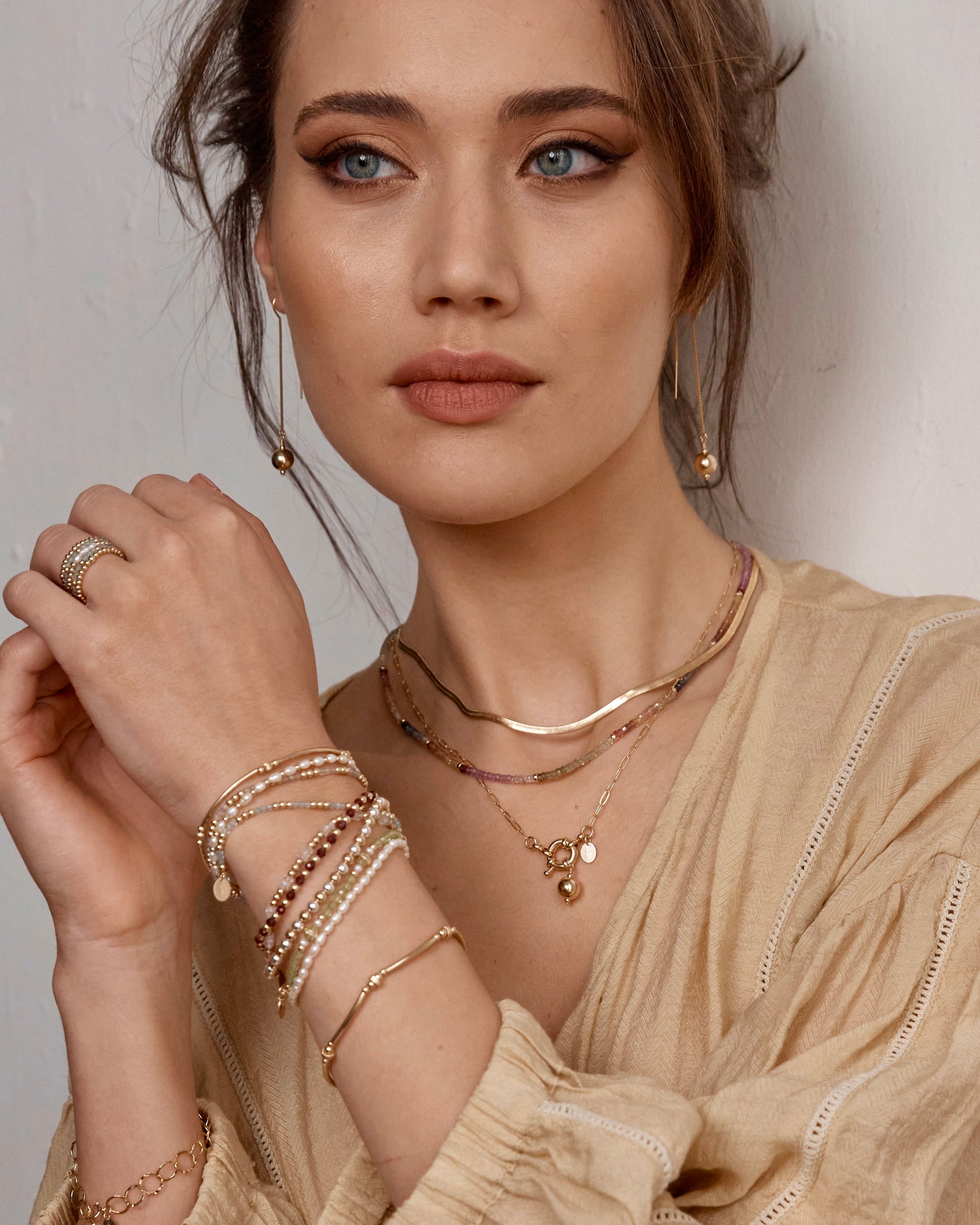 Woman wearing gold gemstone jewellery including necklaces, bracelets, earrings, and rings against a neutral background