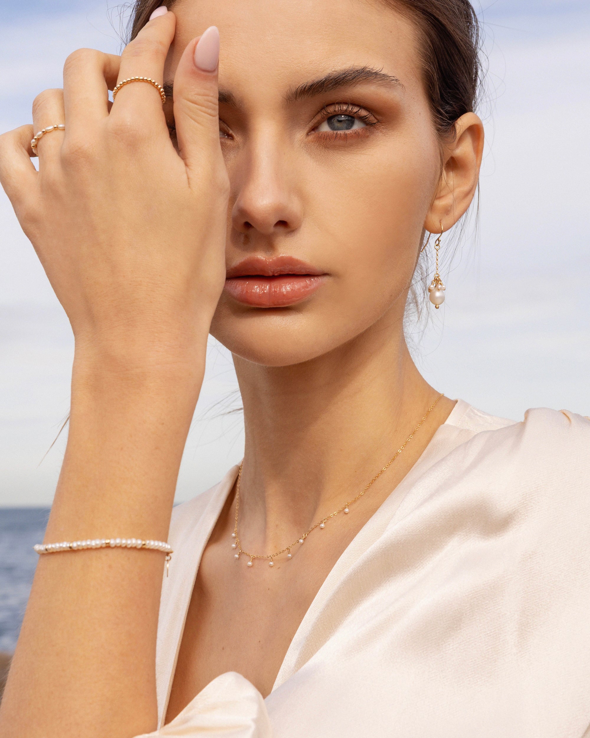 Woman wearing gold pearl jewellery with an ocean background