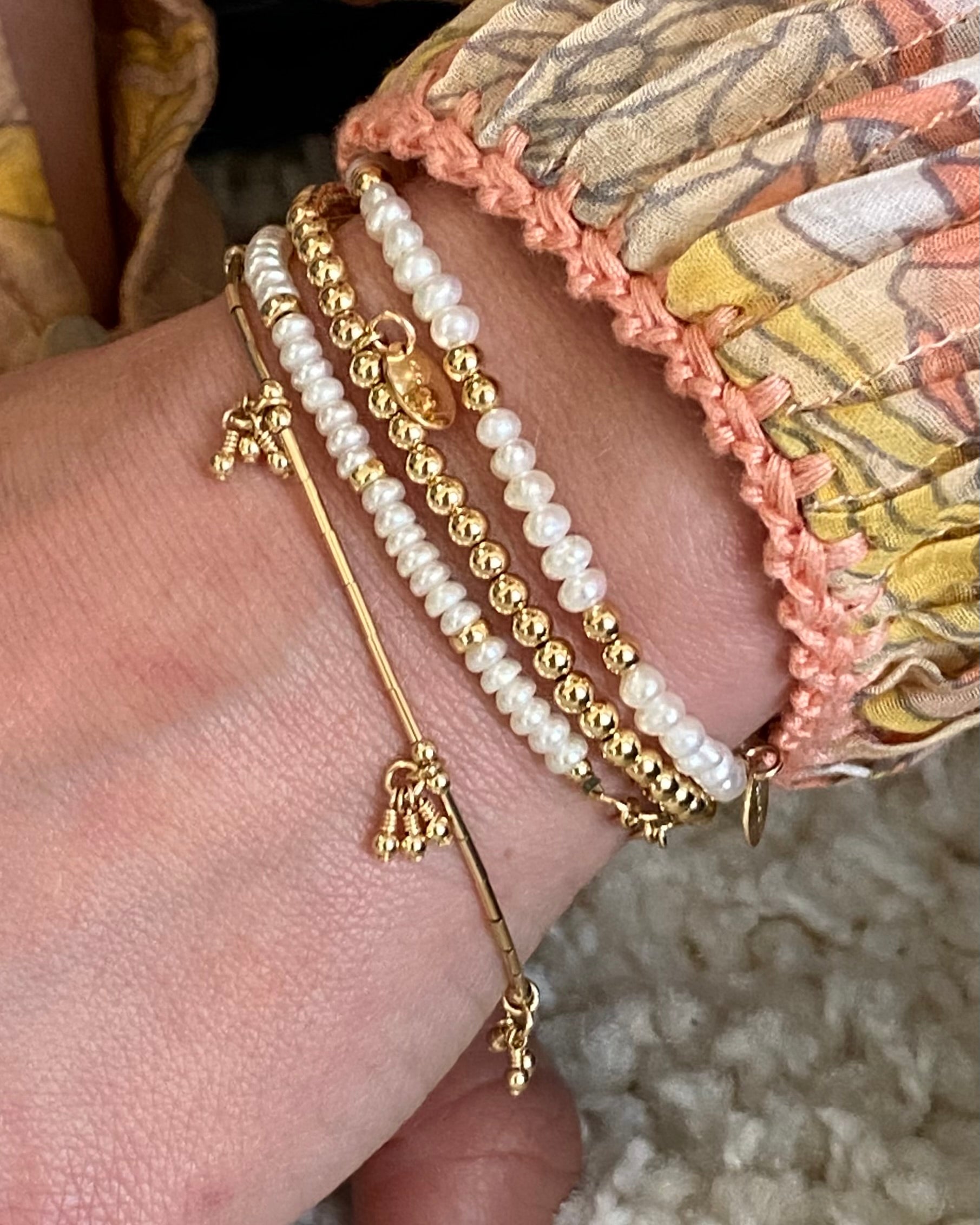 Close-up of a wrist wearing gold and pearl  bracelets with a patterned sleeved blouse.