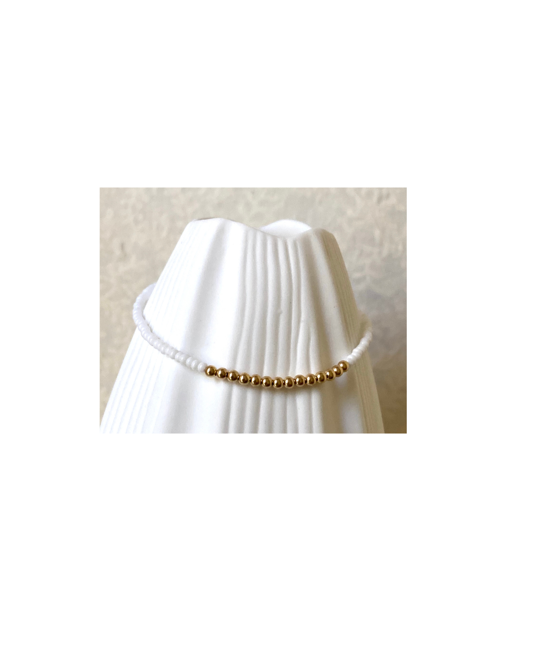 Gold and white glass beaded bracelet on a white vase against a white background