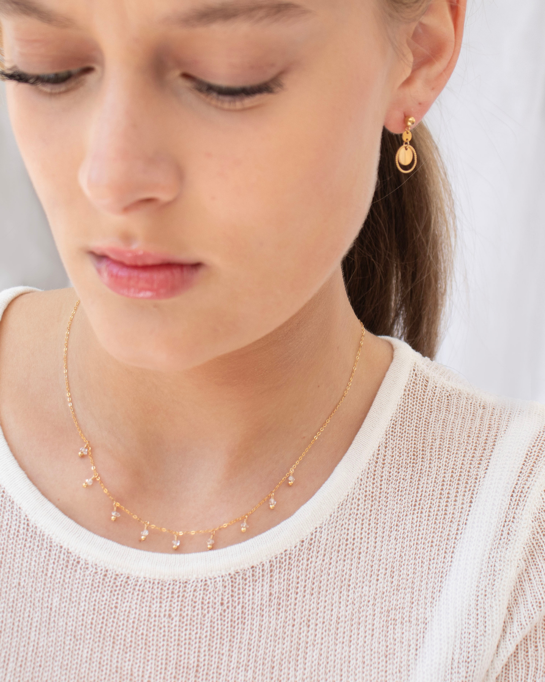 Close-up of a woman wearing gold earrings and a delicate herkimer diamond necklace.
