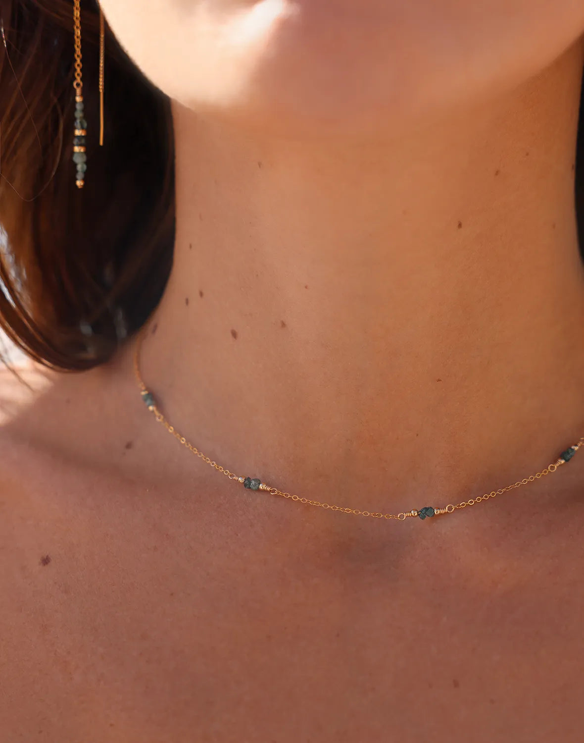 Model wearing gold earrings featuring rare Grandidierite gemstones, accented with gleaming gold beads, suspended from long, sleek gold threads