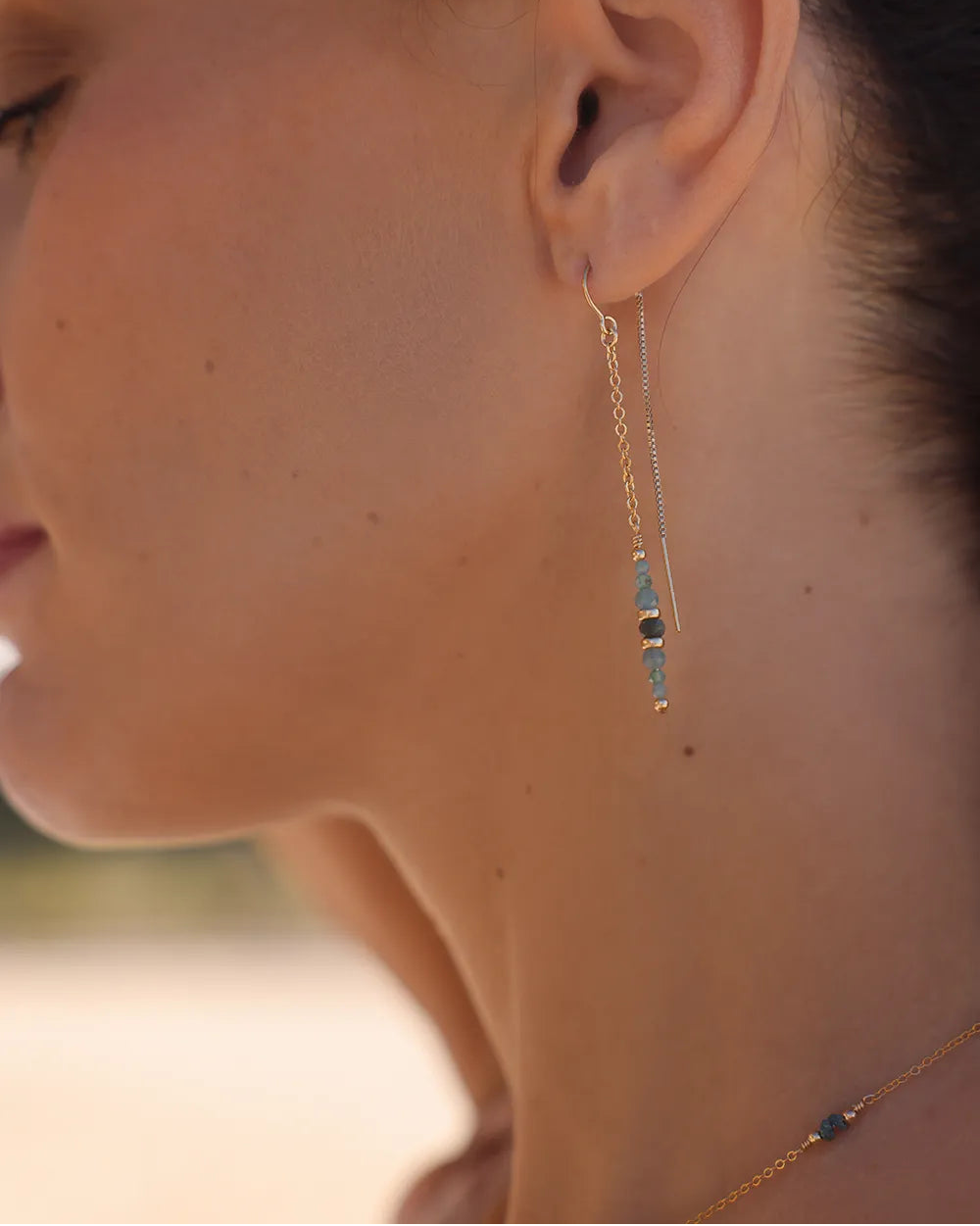 Model wearing gold earrings featuring rare Grandidierite gemstones, accented with gleaming gold beads, suspended from long, sleek gold threads