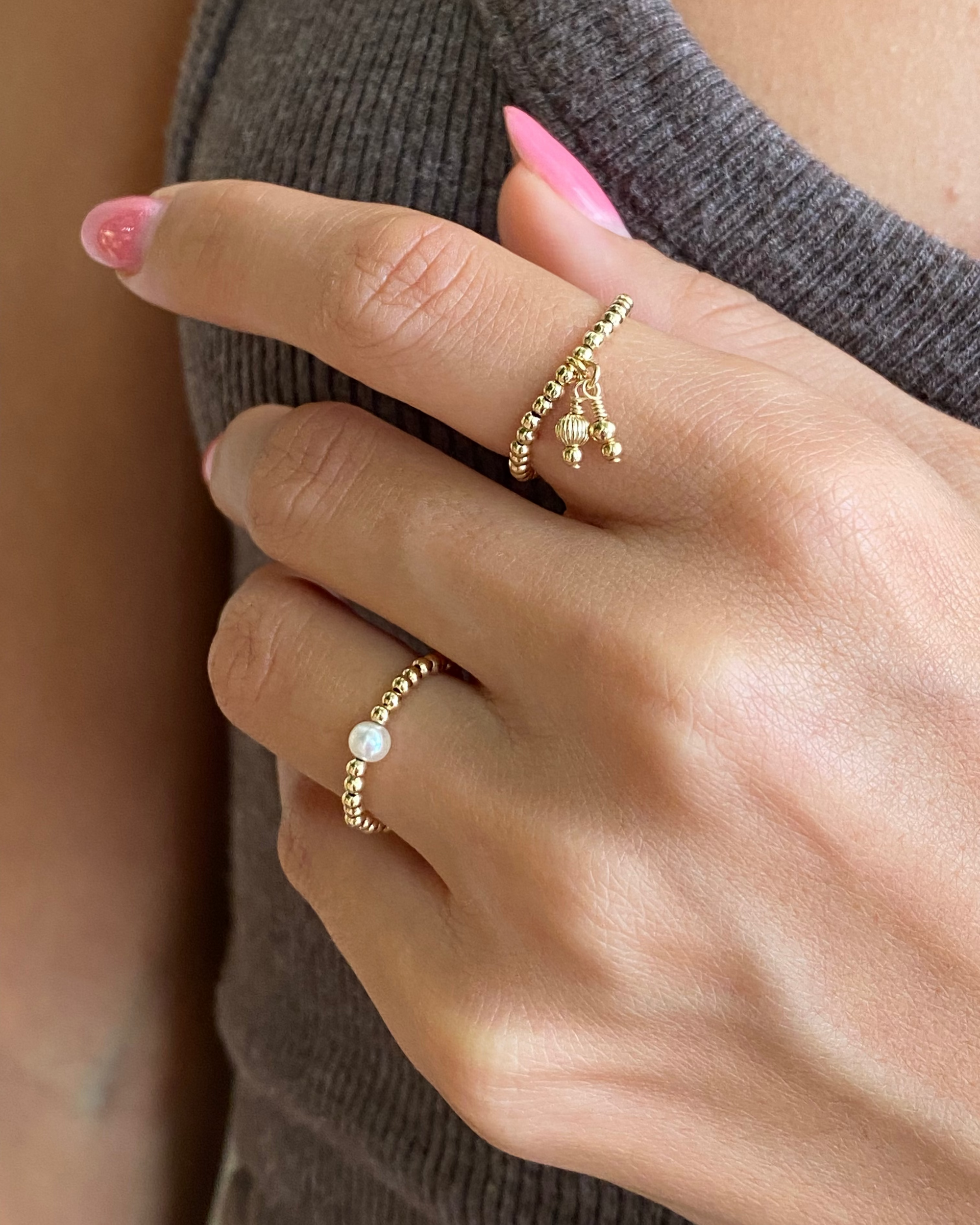 Close-up of a hand wearing two gold rings with pearl-like stones on a neutral background