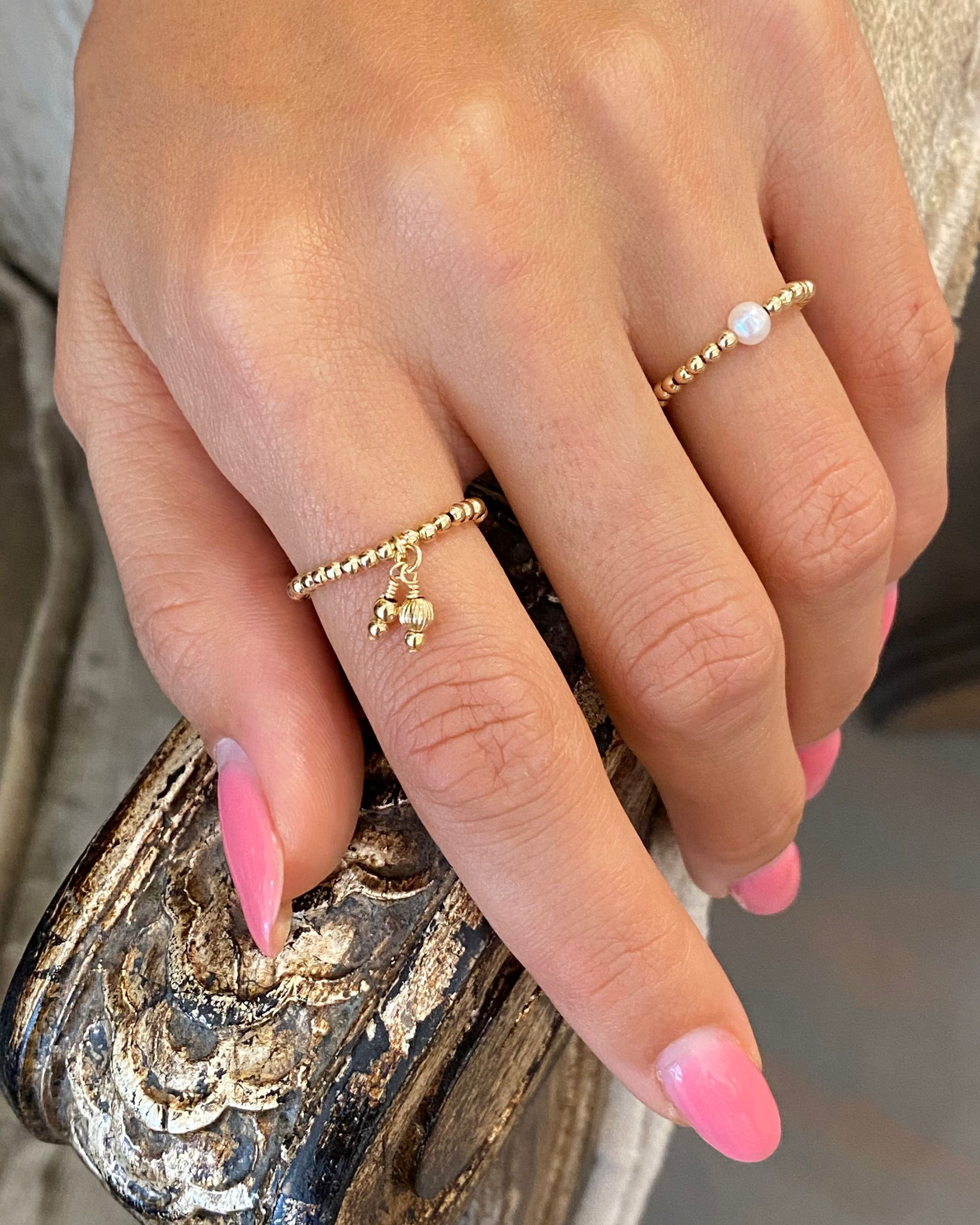 Close-up of a hand wearing gold rings with pink nail polish