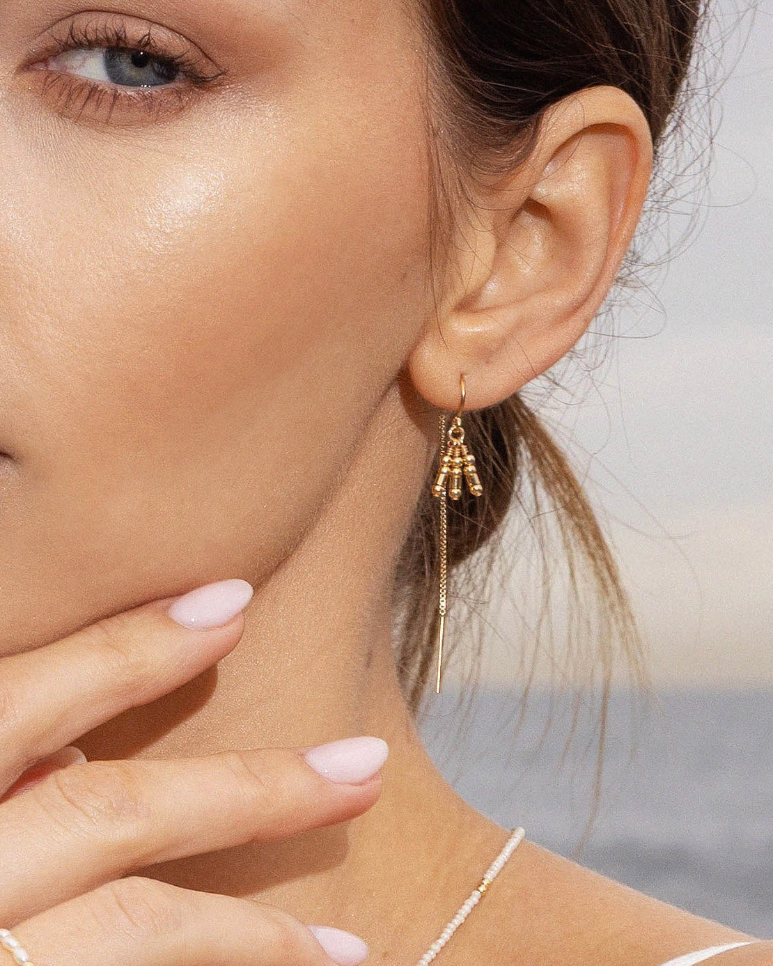 Close-up of a woman wearing gold thread earring with gold beads with a blurred ocean background