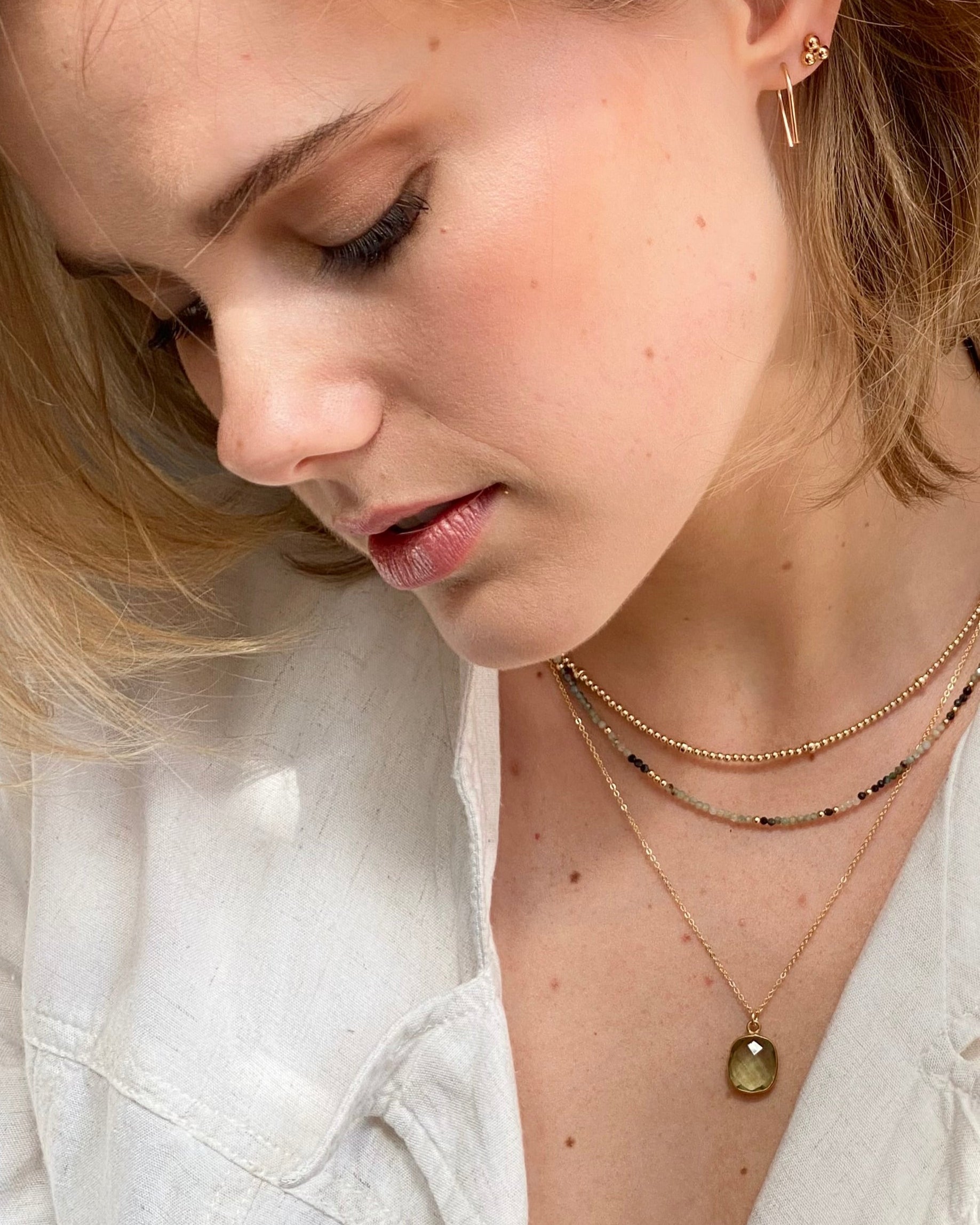 Close-up of a woman wearing layered gold necklaces and earrings with a neutral background