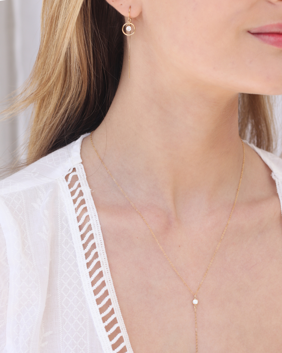 Close-up of a woman wearing a cubic zirconia delicate gold lariat necklace and matching thread earrings.