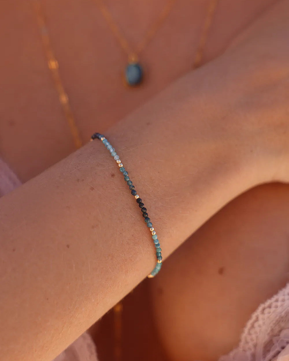 Model wearing bracelet featuring faceted teal blue Tourmaline gems paired with gold accent beads
