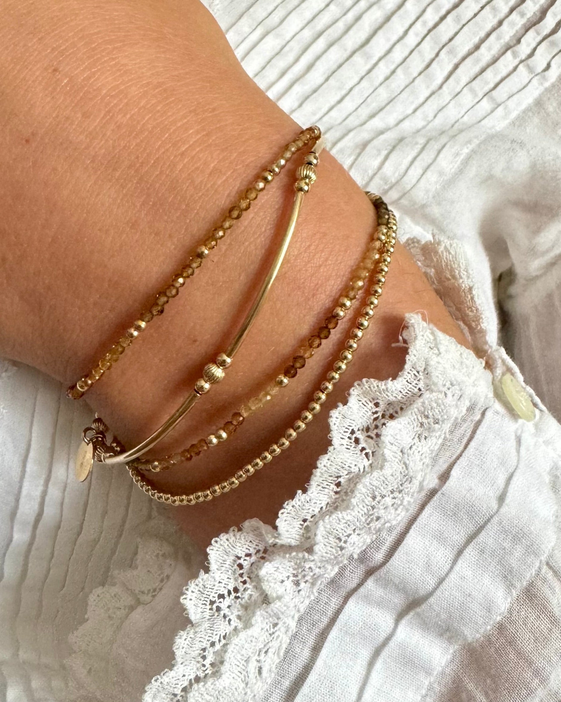 Woman's wrist with gold beaded bracelets stacked with tourmaline gemstone bracelets 