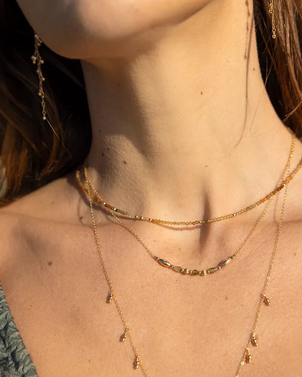 Model wearing necklace featuring faceted Tourmaline gems in rich shades of brown and amber, accented with scattered gold beads