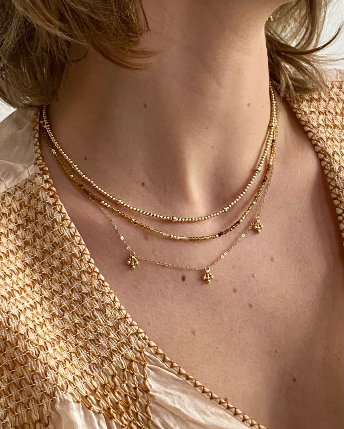 Close-up of a woman wearing a tourmaline gemstone necklace layered with gold necklaces with a textured garment.