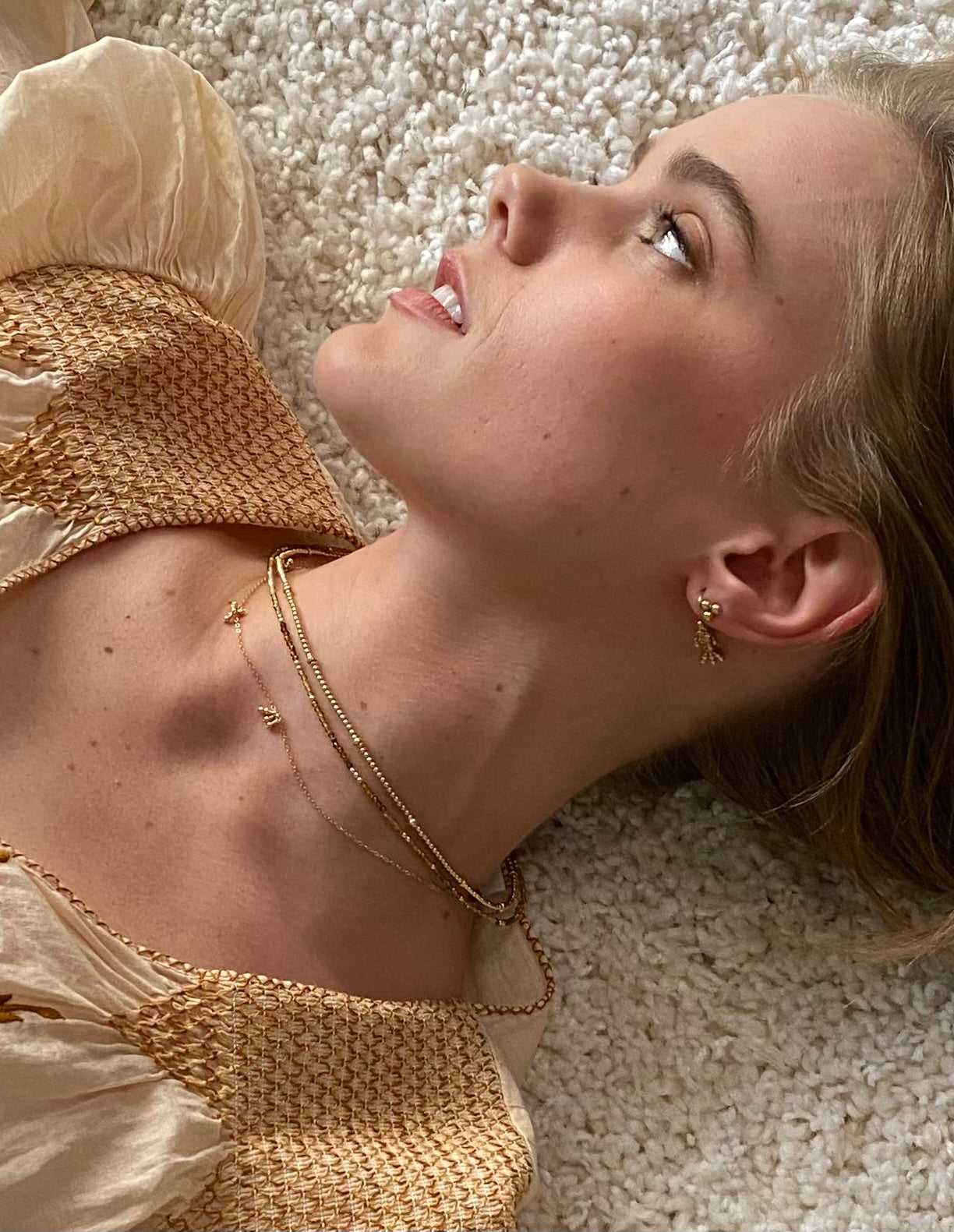 Close-up of a woman and wearing multiple gold necklaces against a neutral background