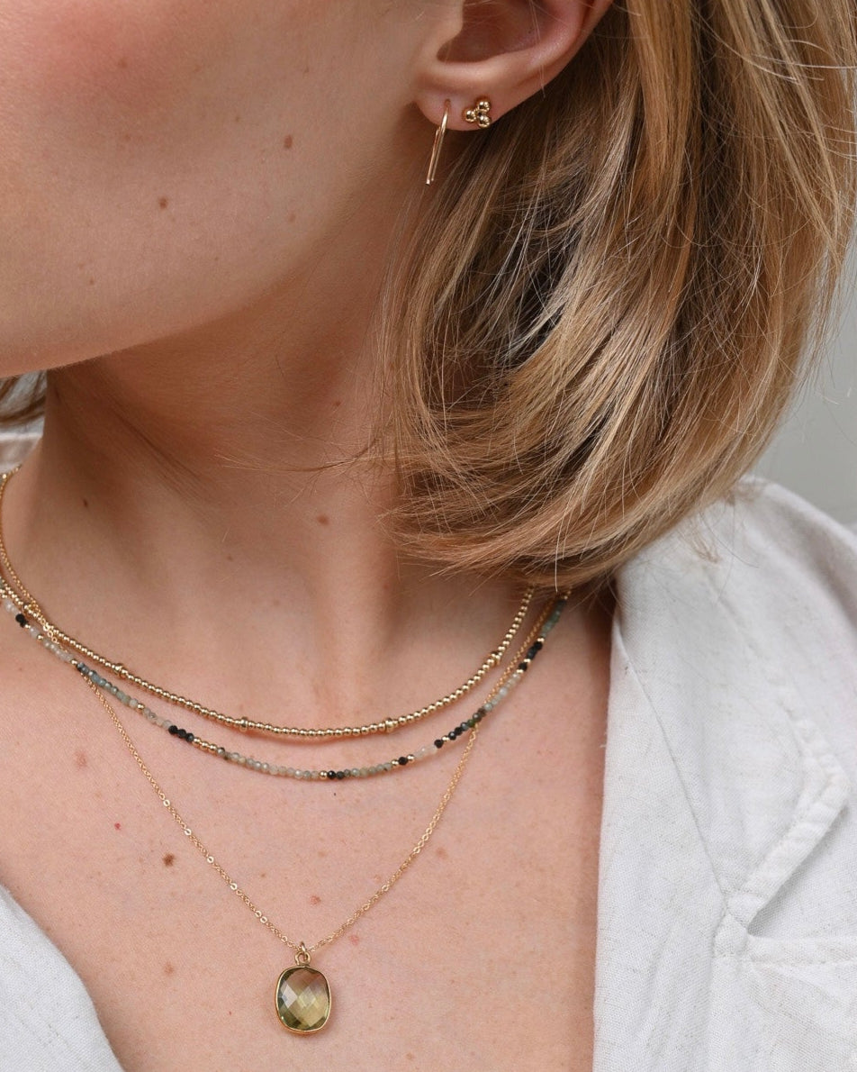 Close-up of a woman wearing gold earrings with layered gemstone necklaces.