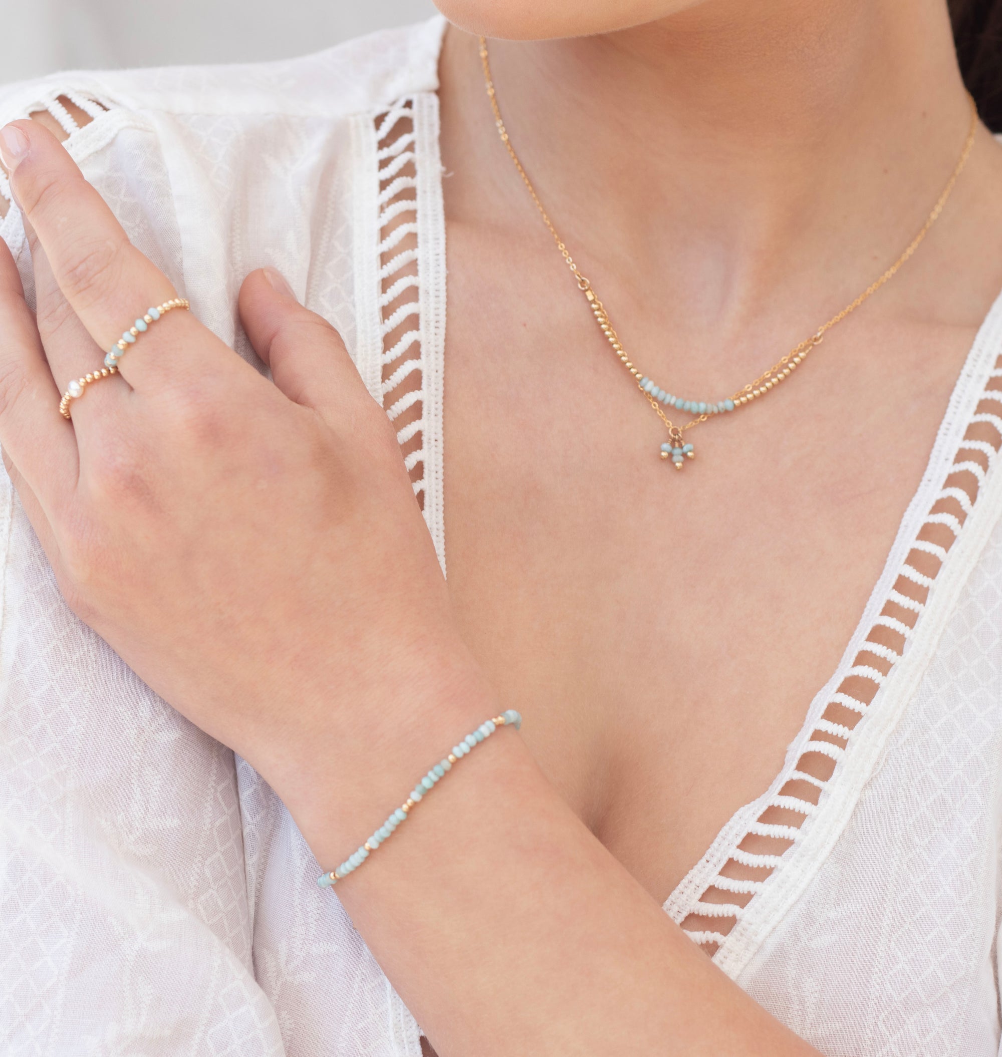 Person wearing a white lace top with gold larimar gemstone necklace, and ring